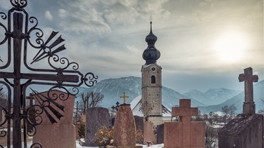 Kirche St. Georg in Ruhpolding mit Friedhof und Bergen im Hintergrund im Winter. | Bild: stock.adobe.com/H. Rambold